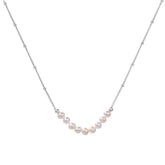 Delicate sterling silver chain necklace with small freshwater pearls arranged in a curved smile arc on cream background.