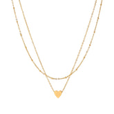Delicate double-chain gold necklace with tiny heart pendant on cream background