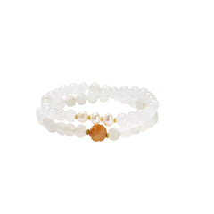 Three layered white beaded bracelets with carved orange agate lotus centerpiece and freshwater pearls on cream background.